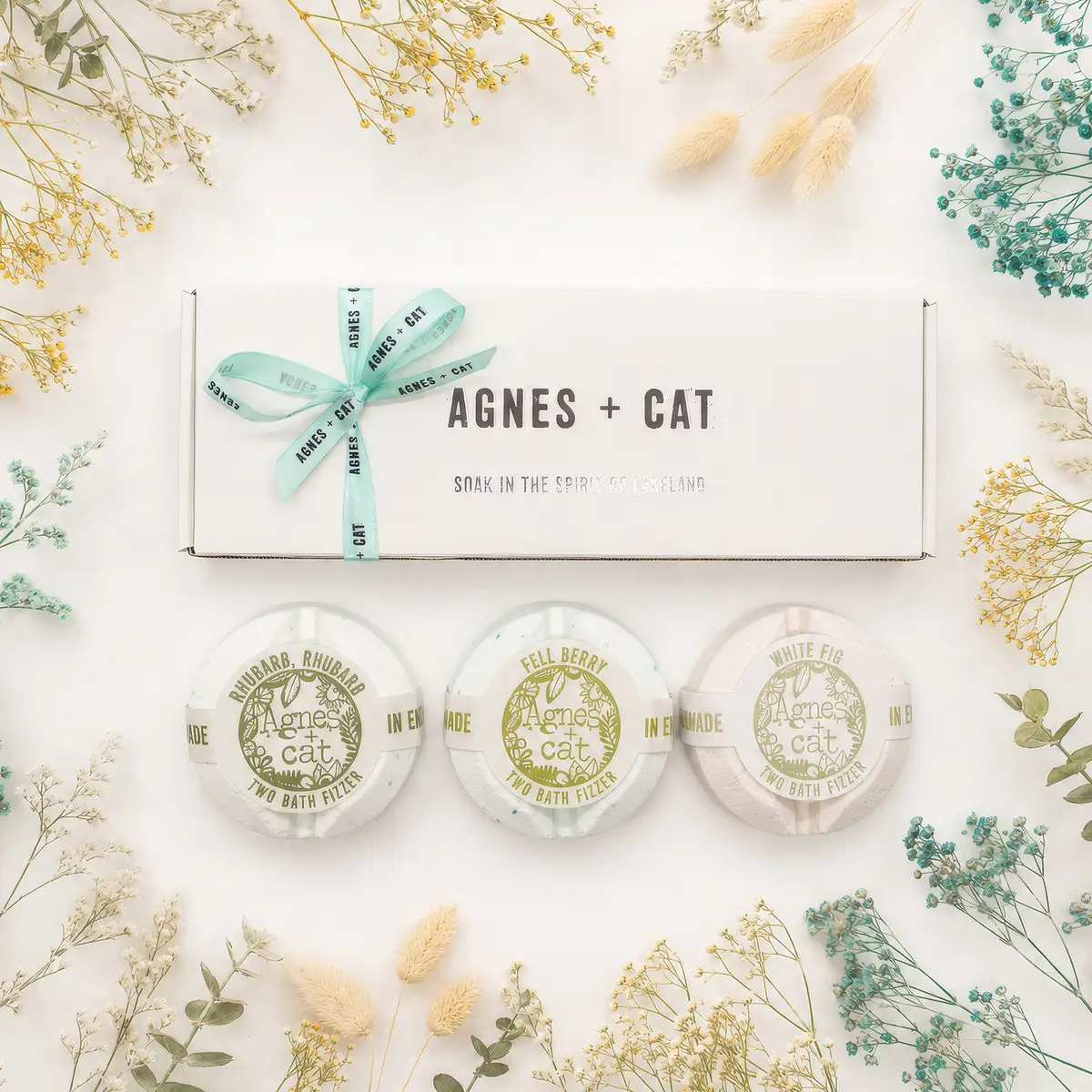 Agnes + Cat presentask med tre badbomber i dofterna rabarber, bär och vitt fikon, omgiven av torkade blommor
