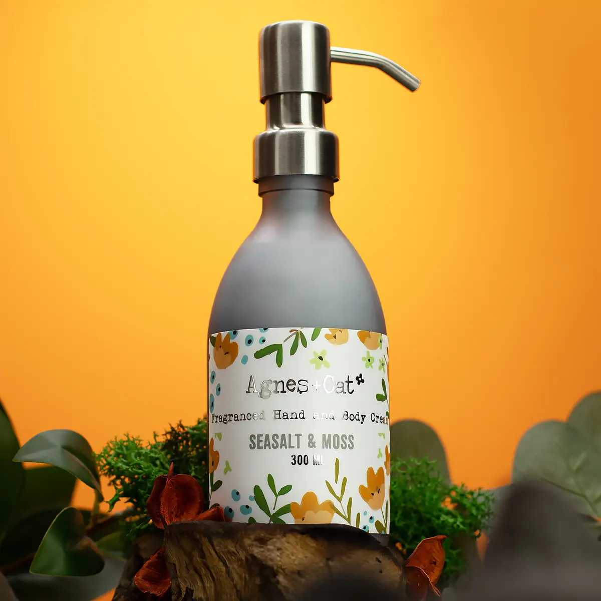Pumpflaska med Agnes + Cat hand- och kroppskräm Sea Salt & Moss 300 ml mot orange bakgrund