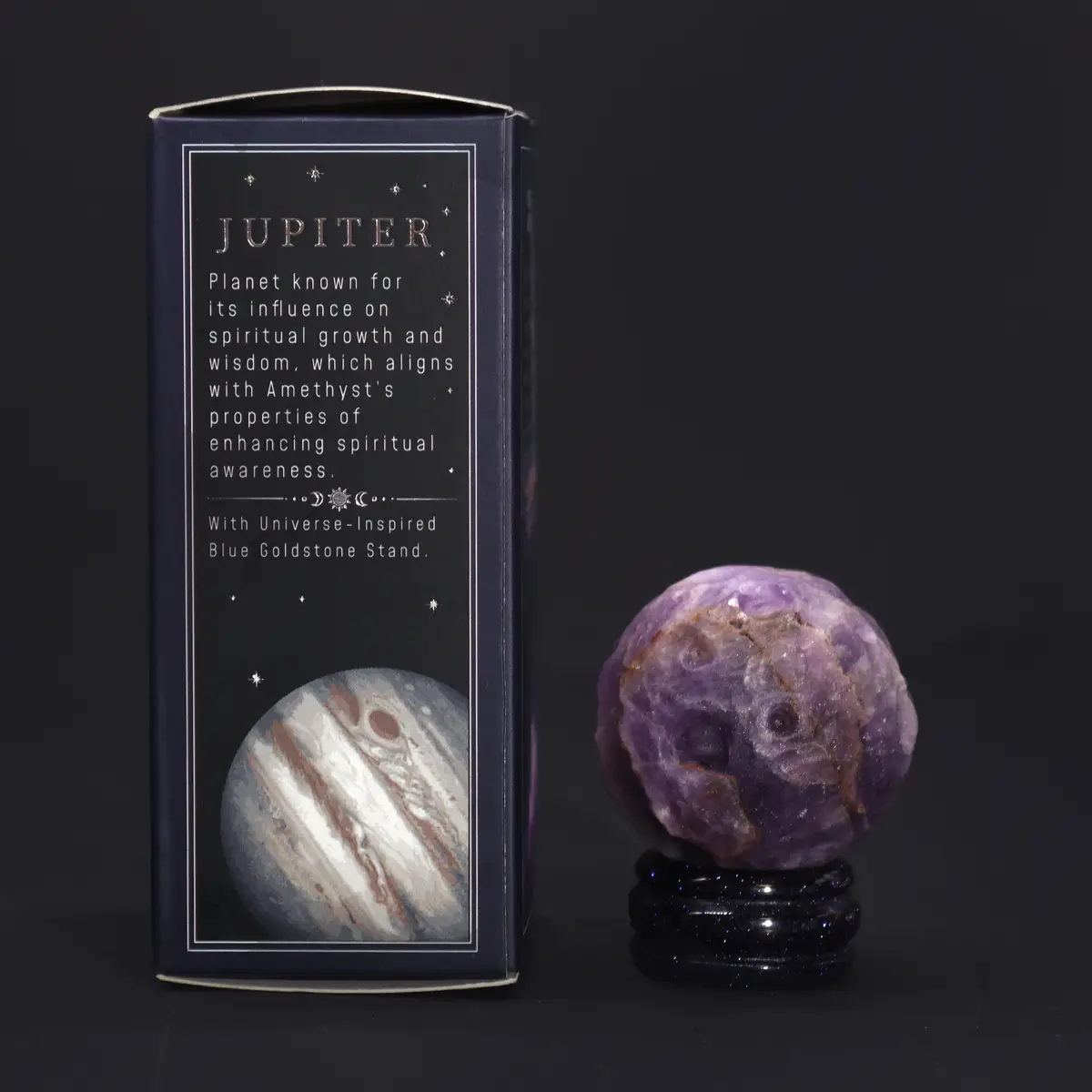 Ametistklot på blått guldkristallstativ bredvid förpackning med Jupiter-motiv