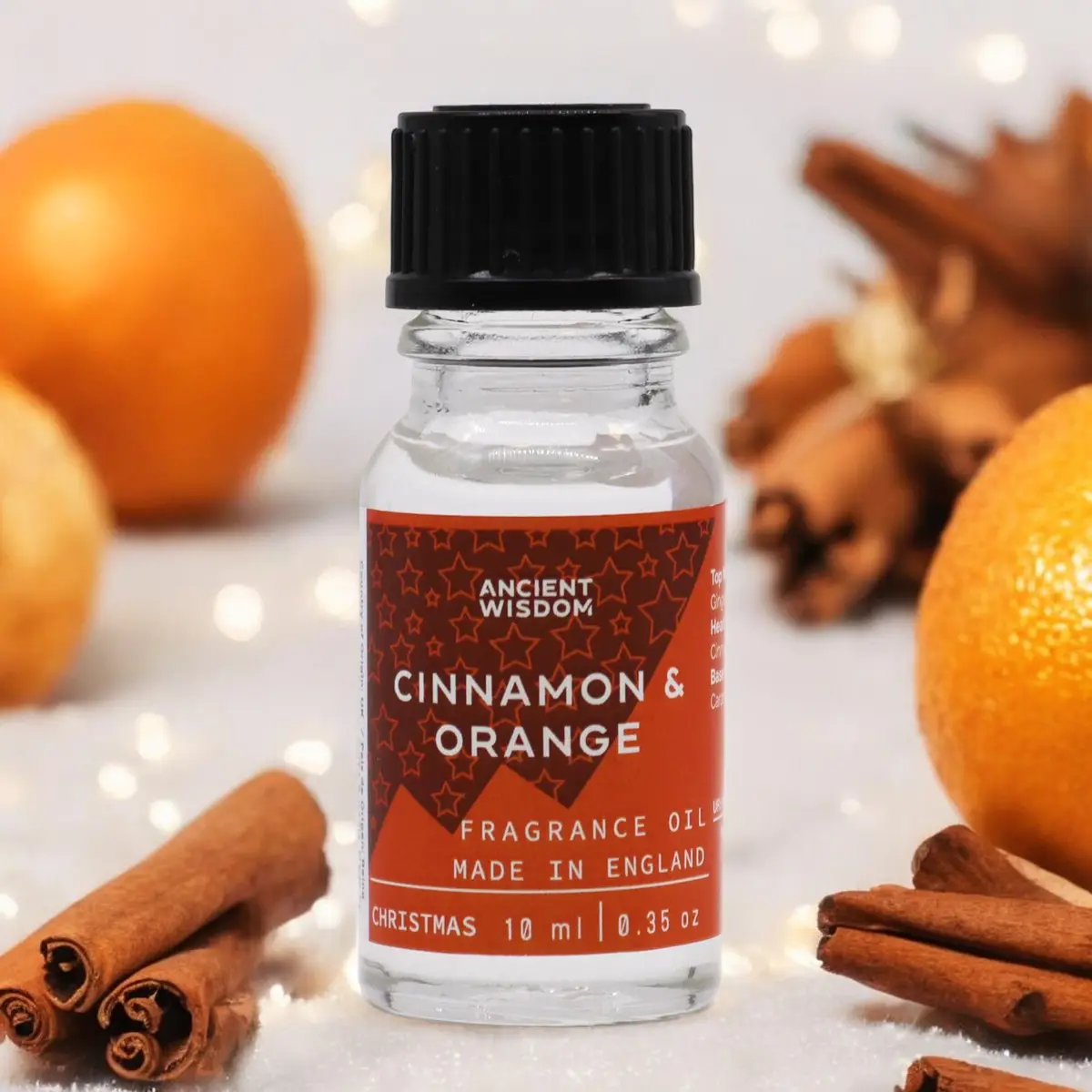Flaska med Ancient Wisdom doftolja kanel och apelsin 10 ml omgiven av kanelstänger och apelsiner