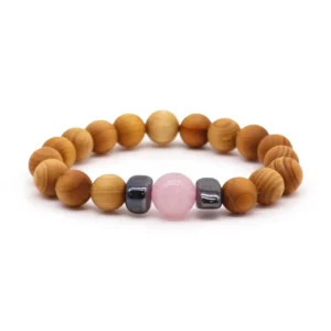 Armband i cederträ med en rosa rosenkvarts-pärla och två mörka pärlor på vit bakgrund