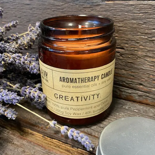 Brunt glasljus med etikett Aromatherapy Candle Creativity och lavendel vid sidan