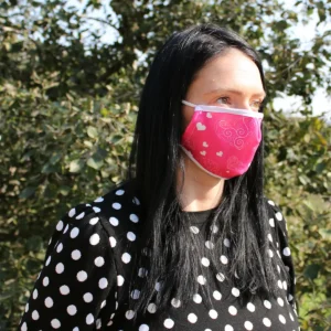 Vuxen kvinna som bär en rosa återanvändbar ansiktsmask med hjärtan utomhus