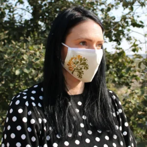 Vuxen kvinna med svart hår som bär en återanvändbar ansiktsmask med gyllene trädmönster utomhus