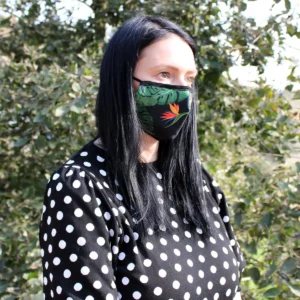 Vuxen kvinna med svart hår som bär en återanvändbar ansiktsmask med grönt djungelmönster och justerbara elastiska band