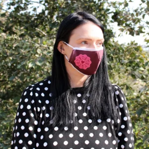 Vuxen kvinna med svart hår som bär en röd återanvändbar ansiktsmask med mandalamönster och hjärta