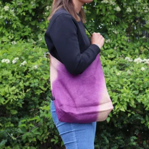 Axelväska i mjuk blandning antique fuchsia med batikmönster, buren av person i svart tröja och blå jeans