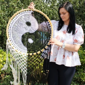 Kvinna håller en stor handgjord Bali drömfångare med svartvit Ying Yang-design i trädgård