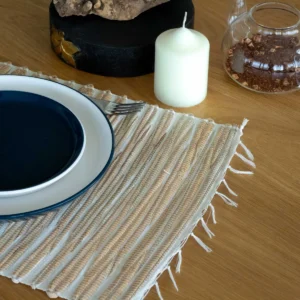 Bordstablett i vattenhyacint med fransar på ett träbord med tallrikar och ljus