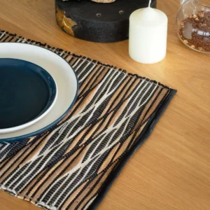 Bordstablett i vattenhyacint med svartvita vågmönster på ett träbord med tallrikar och ljus