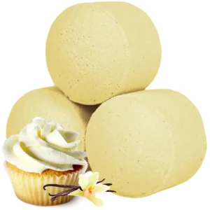 Tre runda badbomber i ljusgul färg med vaniljcupcake och vaniljblomma i förgrunden
