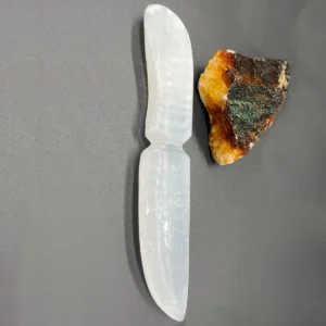 Ceremoniell kniv i vit selenit på grå bakgrund med rå kristall