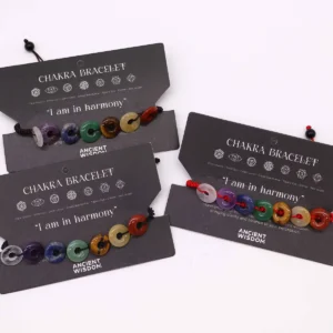 Chakra-armband i tråd med små donutformade ädelstenspärlor i olika färger på svart kort