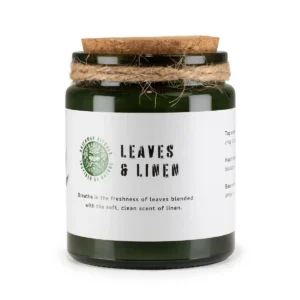 Grönt glasljus med korklock och vit etikett med texten Leaves & Linen