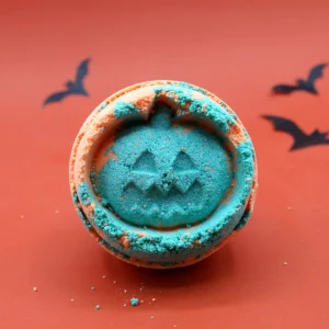 Orange och blå badbomb formad som en Halloweenpumpa på orange bakgrund med fladdermöss