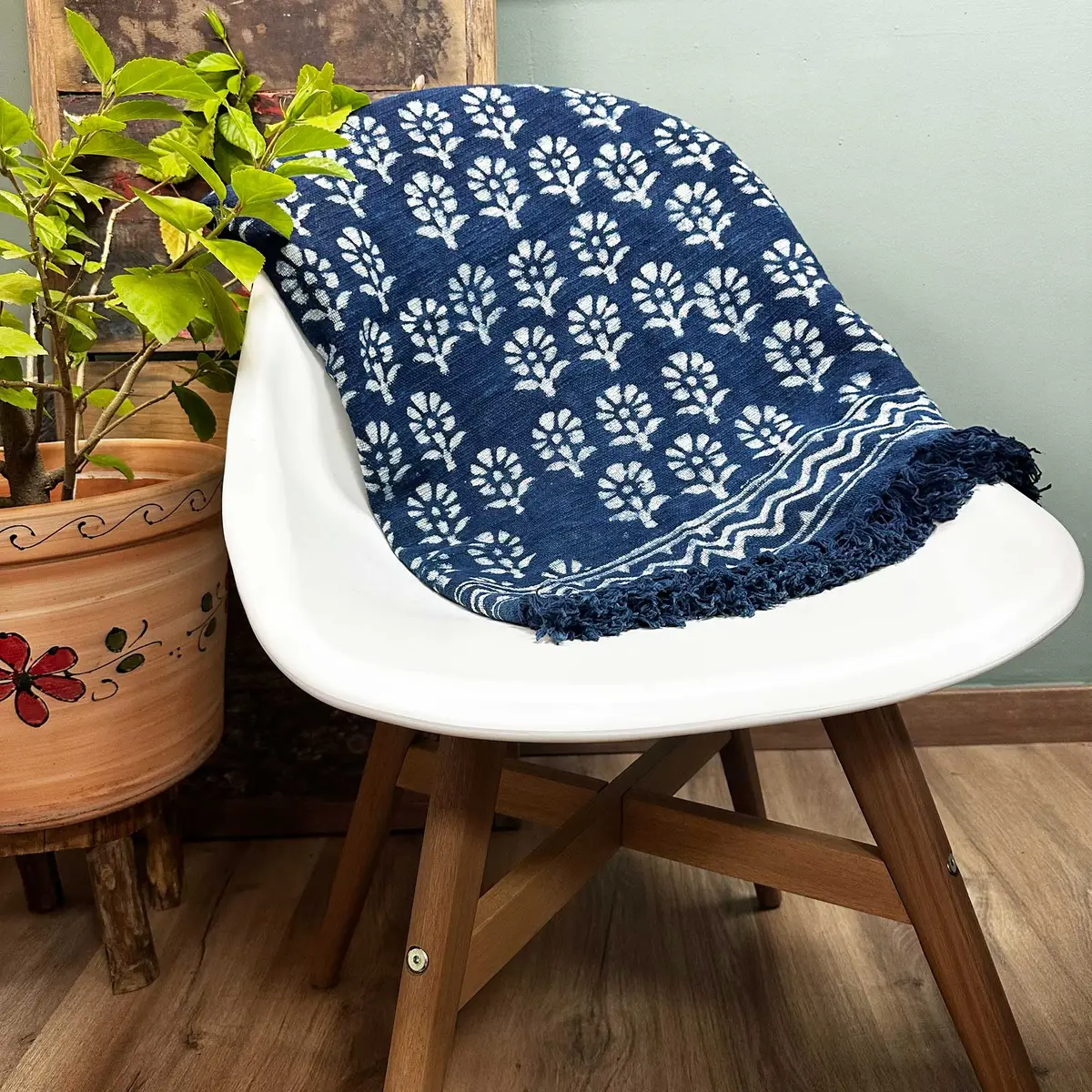 Indigoblå pläd med vitt blommönster och fransar på vit stol i inomhusmiljö