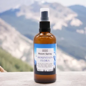 Brun flaska med rumsspray Mountain Flora framför suddig bergslandskap
