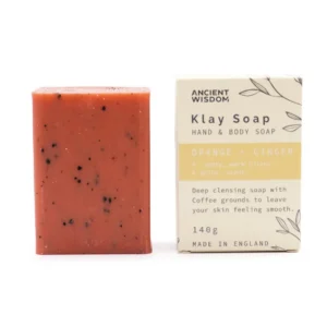 Rödbrun tvål med svarta kaffebönor bredvid förpackning med text Klay Soap Orange + Ginger