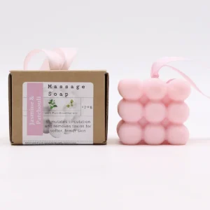 Rosa massage-tvål med bubbelstruktur och rosa band bredvid brun kartongförpackning