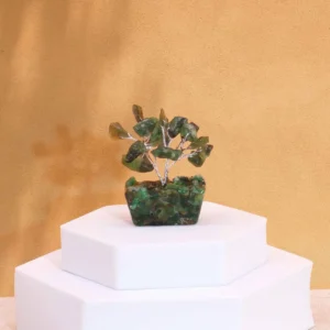 Miniatyrträd av grön aventurin på orgonitbas placerad på vit piedestal