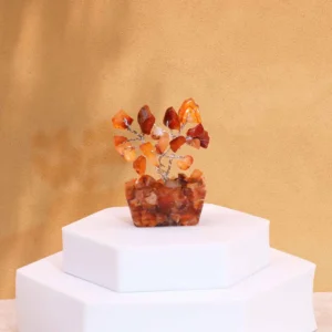 Miniatyrträd av karneolstenar på orgonitbas placerat på vit piedestal