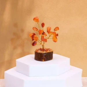 Miniatyrträd med orange karneolstenar på träbas placerat på vit piedestal