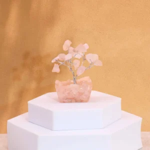 Miniatyrträd av rosenkvarts på orgonitbas placerat på vit piedestal