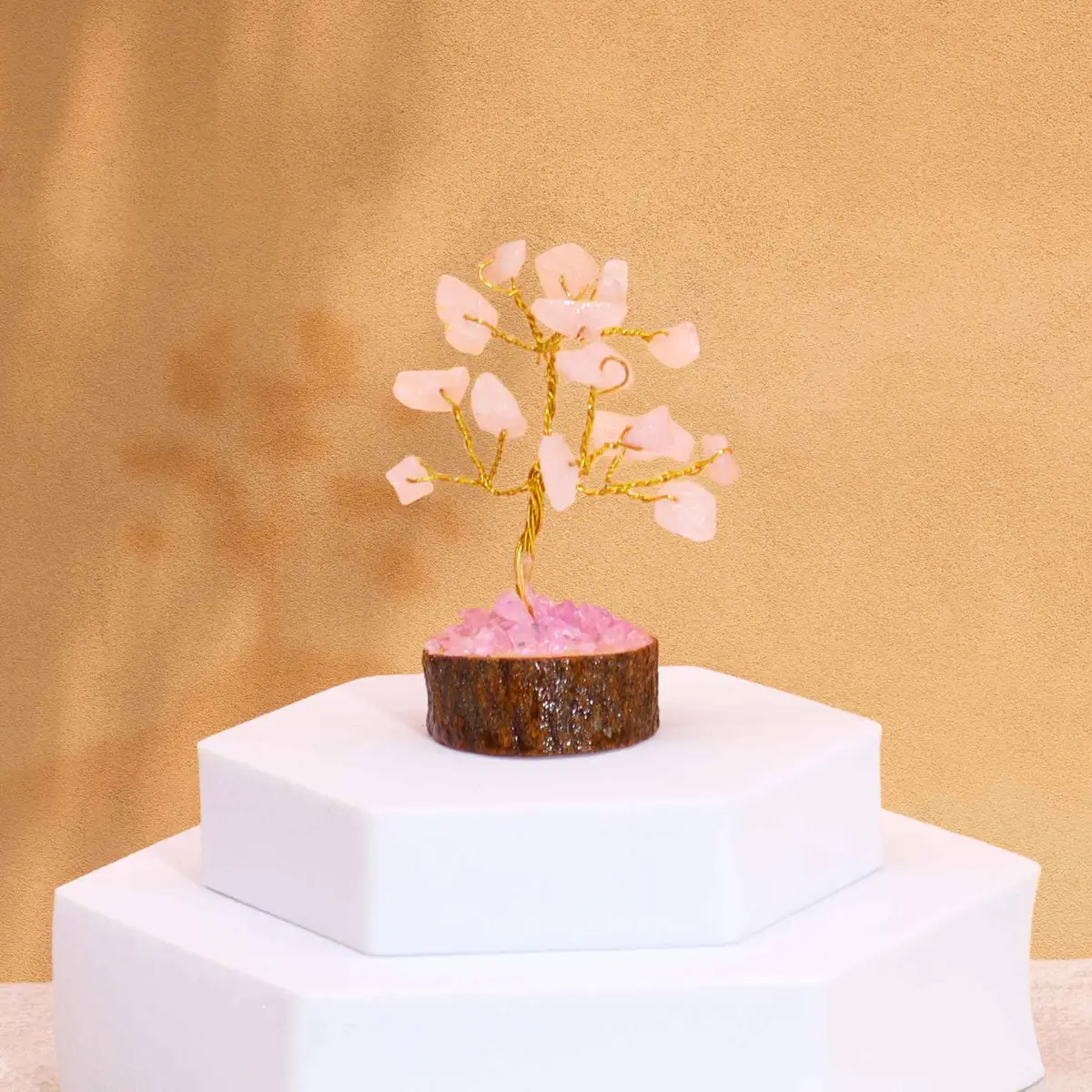 Miniatyrträd med rosa rosenkvartsstenar på träbas placerat på vit piedestal