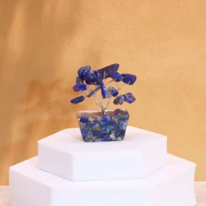 Miniatyrträd av blå sodalit på orgonitbas placerat på vit piedestal