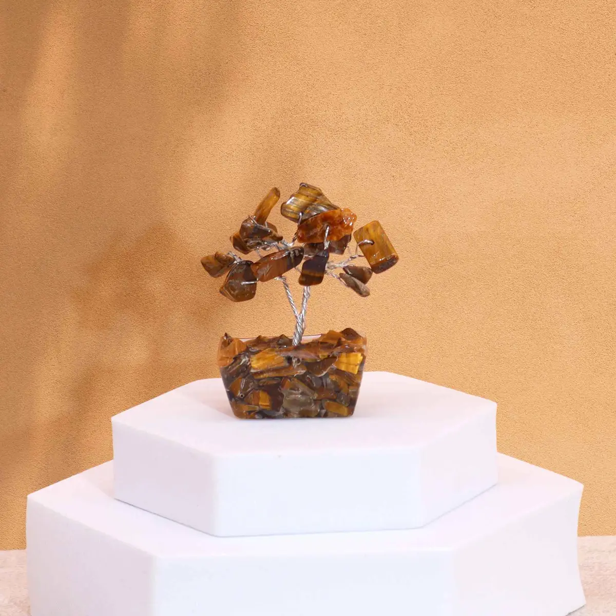 Miniatyrträd av tigeröga på orgonitbas placerat på vit piedestal