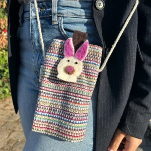 Randigt mobilfodral med filtkanindekor hängande runt midjan på person i jeans och kavaj