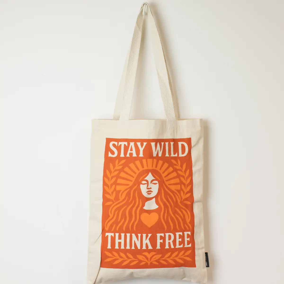 Naturlig bomullstygkasse med orange tryck och texten Stay Wild Think Free