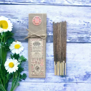 Förpackning med ritualhartser på pinne och kamomillblommor på träyta