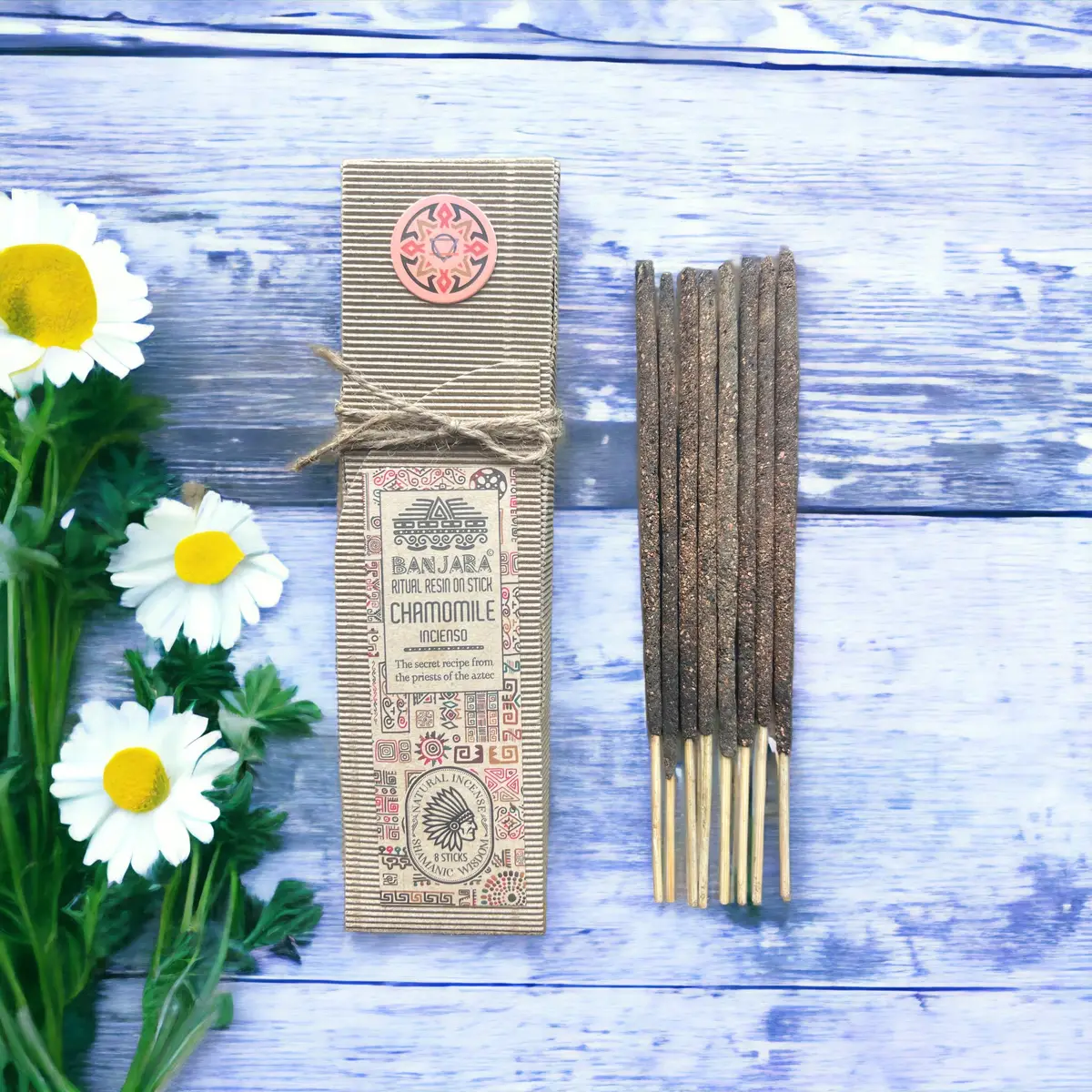 Förpackning med ritualhartser på pinne och kamomillblommor på träyta