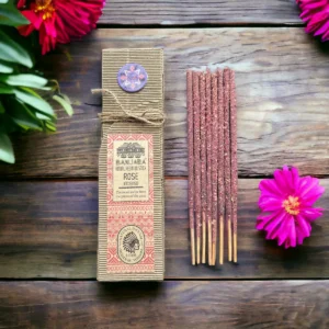 Förpackning med ritualhartser på pinne och rosdoft bredvid rosa blommor på träbord