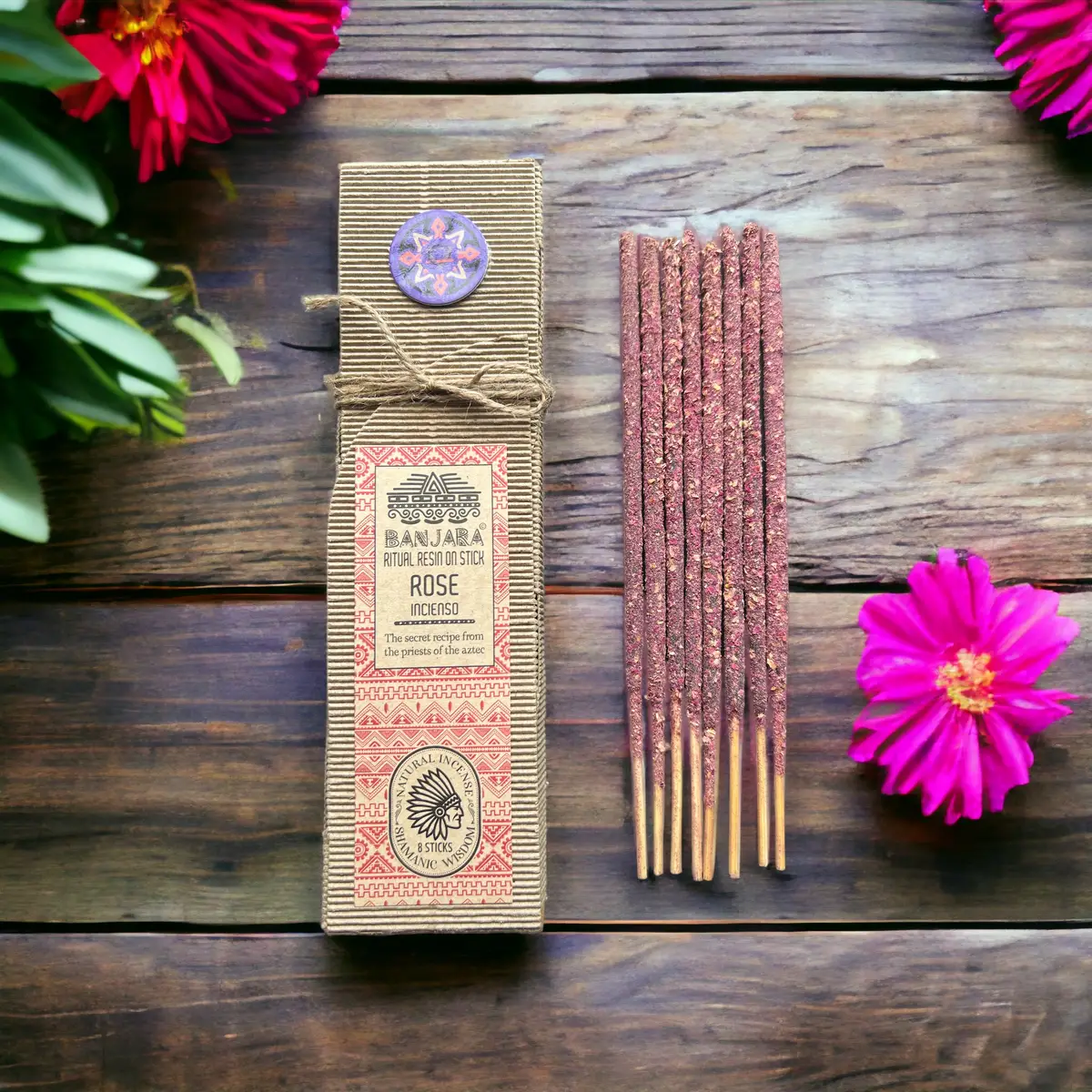 Förpackning med ritualhartser på pinne och rosdoft bredvid rosa blommor på träbord