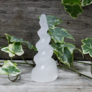 Spiralformat selenittorn i form av ett enhörningshorn placerat på träyta med gröna blad runtom