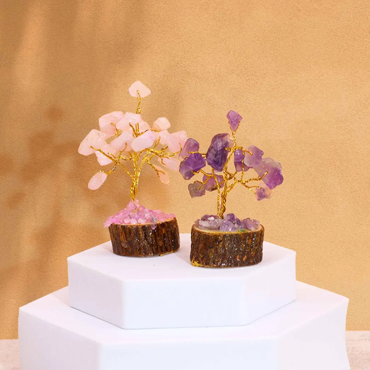Två miniatyrträd av ädelstenar på träbas, en med rosenkvarts och en med ametist, placerade på vit piedestal