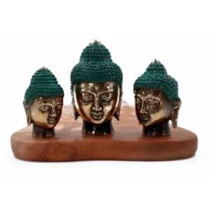 Tre buddhahuvuden i mässing med grön patina på håret placerade på en träplatta