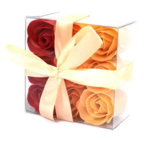 Nio tvålblommor i persikorosa nyanser i en transparent presentask med sidenband