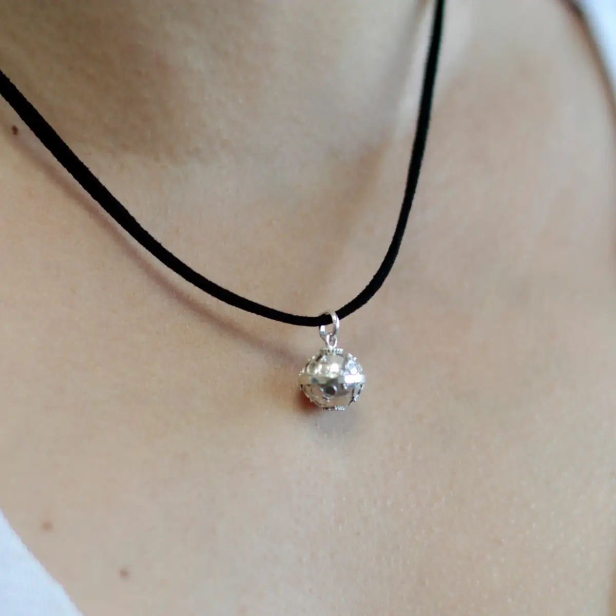 Närbild på silveränglarskälla i silver hängande på svart halsband runt hals