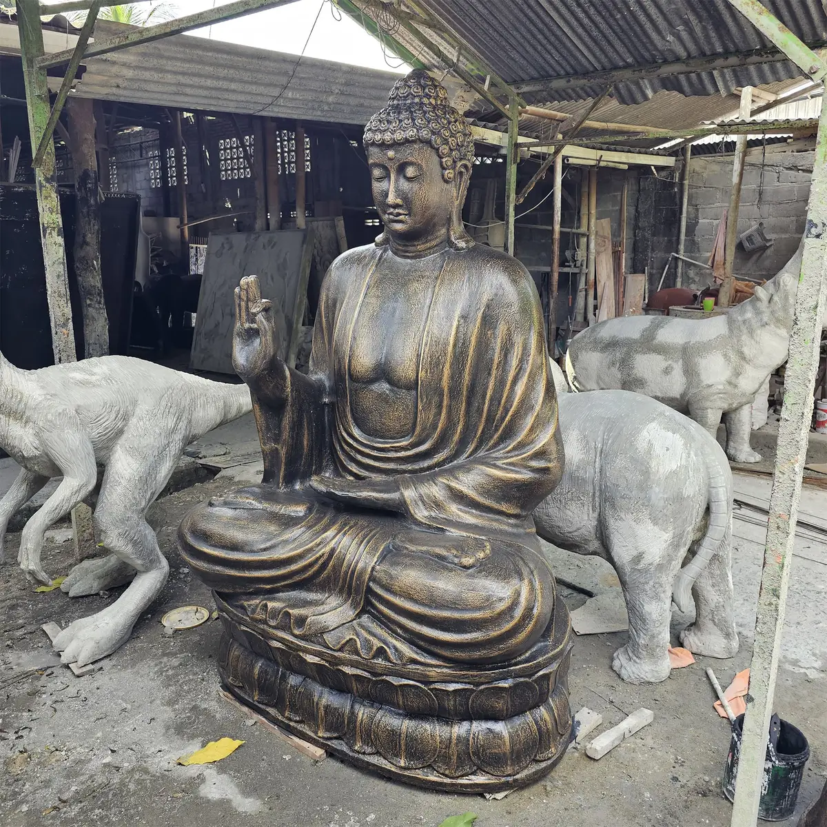 Stor Buddha-staty i antikgul färg sittande på lotus i en verkstadsmiljö