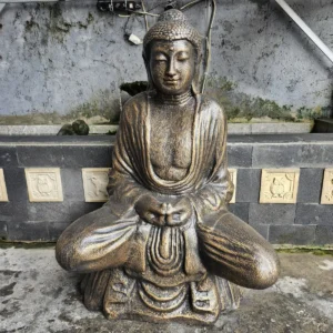 Stor antikgul buddha-staty i sittande meditationspose framför en vägg med dekorativa plattor