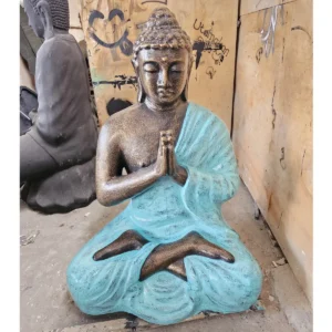 Stor bönande Buddha-staty i turkos och guld placerad i en utomhusmiljö