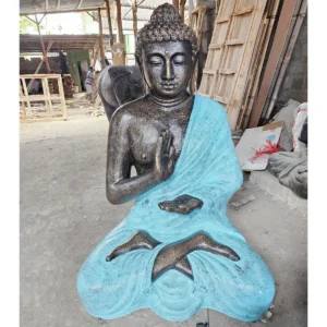 Stor Buddha-staty i turkos och sten med meditativ pose i en verkstadsmiljö