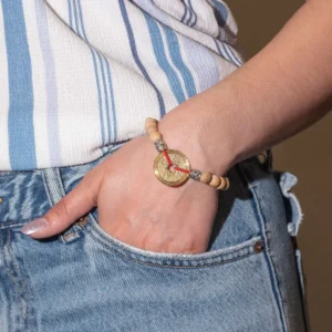 Hand med Tri Hita Karana-armband med träpärlor och guldfärgad symbol på röd tråd