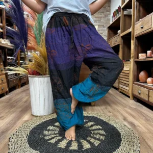 Person som bär lila, svart och blå yoga- och festivalbyxor med Himalaya-mönster i ett rum med träinredning