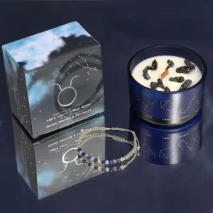 Zodiakljus i blå glasburk med stjärntecken och armband med blå och gröna ädelstenar bredvid förpackning