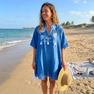 Kvinna i blå strandkaftan med krämfärgad brodyr och tofsar på sandstrand vid havet