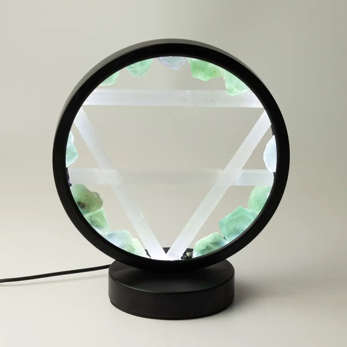 Rund lampa med svart ram och bas, dekorerad med gröna aventurinstenar och vita selenitstavar